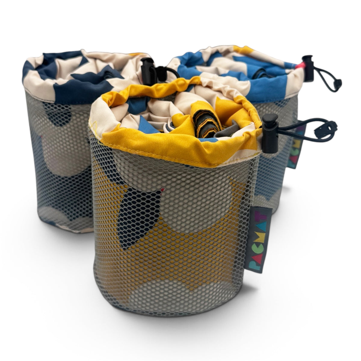Three cylindrical mesh laundry bags with drawstring tops, shown on a clean white background. The bags feature a gray and navy blue camouflage pattern on the exterior and a yellow, blue, and beige pattern on the interior lining.